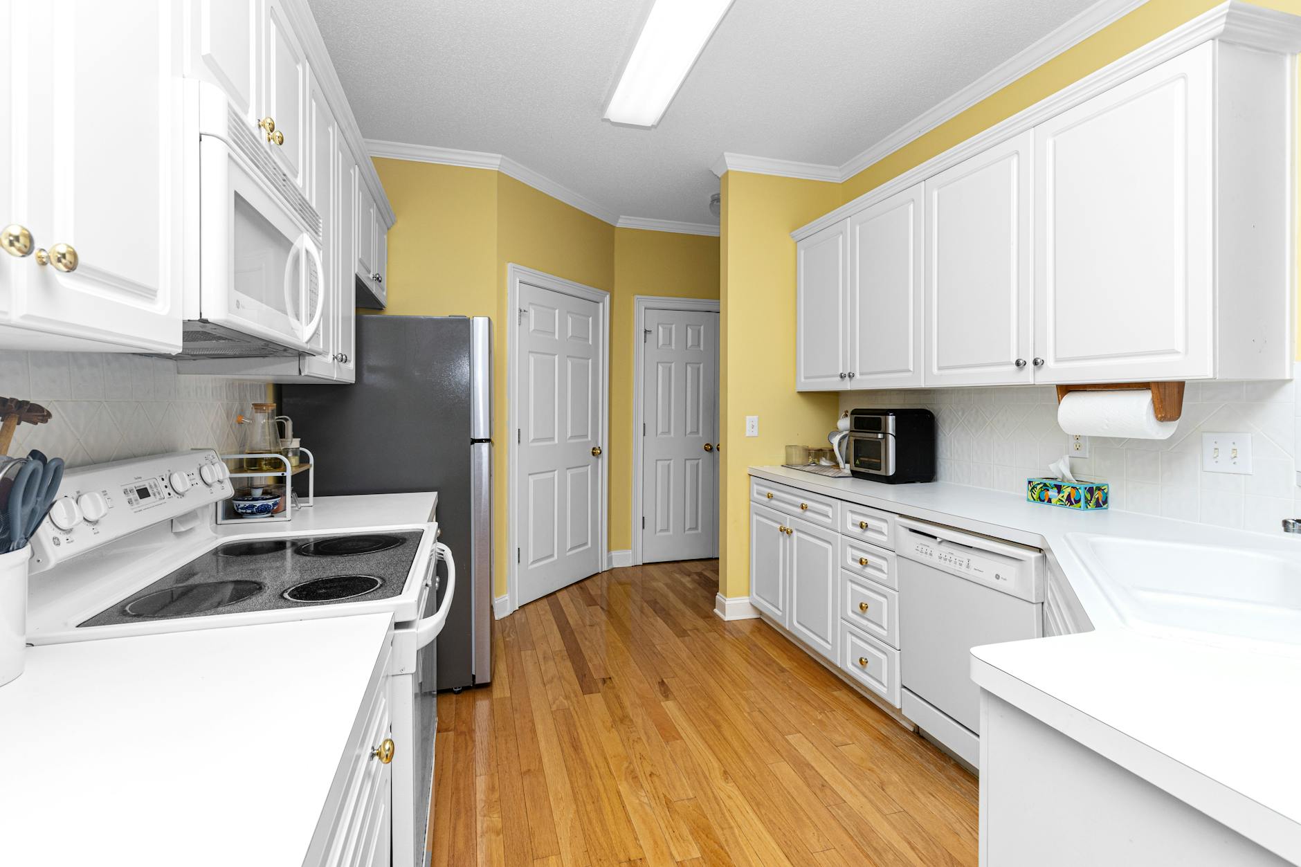 Spacious kitchen with white cabinets, wooden floor, and modern appliances.